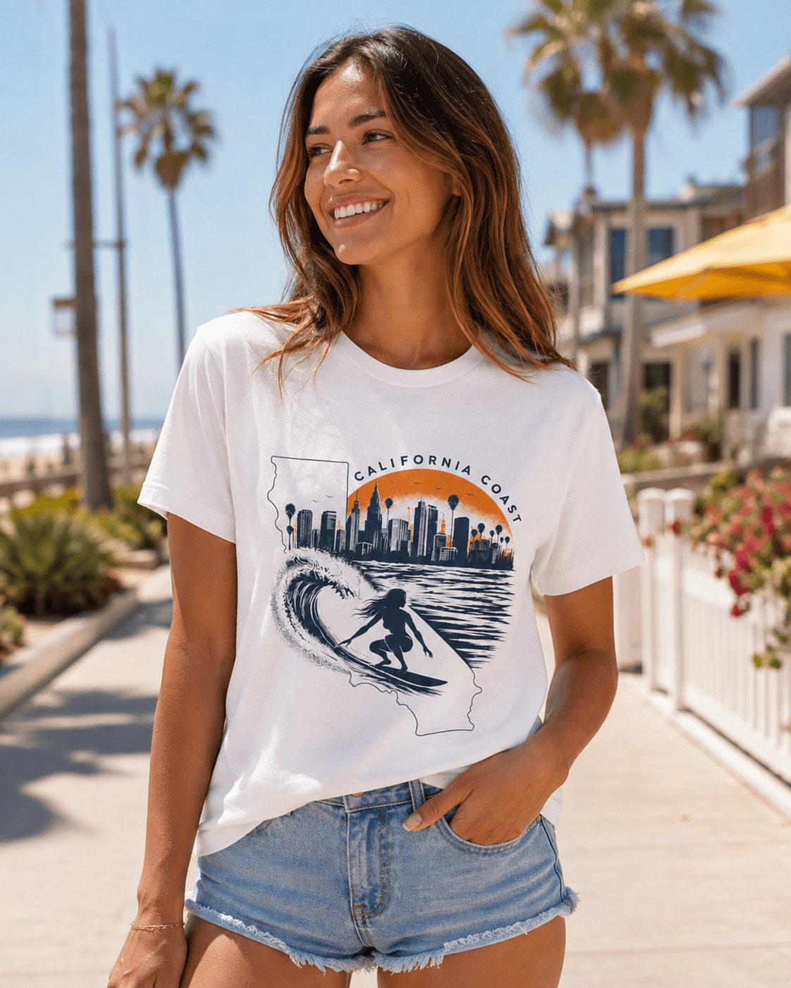 White graphic T-shirt featuring California coast skyline and wave surfer print, worn