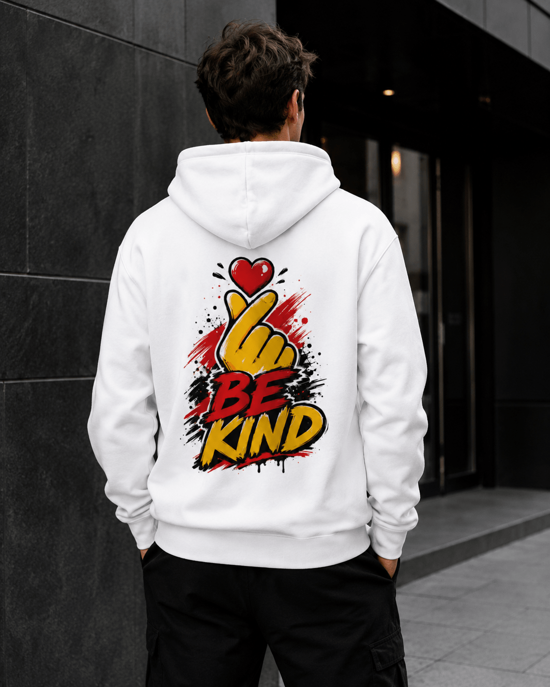 White hoodie worn from behind with 'Be Kind' heart-and-hand graphic