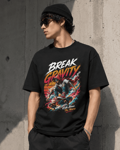 A man wearing a black beanie, sunglasses, and a black graphic t-shirt with a colorful 'Break Gravity' skateboarding design, standing against a concrete wall.