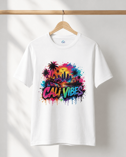 A white short-sleeve crewneck t-shirt hanging on a wooden hanger against a white wall. The shirt features a colorful graphic print on the front with palm trees, a city skyline, a sunset, and the text 'CALI VIBES' in a graffiti-style font.