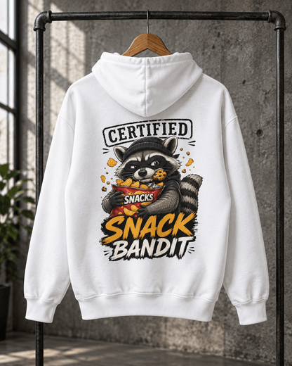Back view of a white pullover hoodie hanging on a wooden hanger against a concrete wall, featuring a back print of a masked raccoon holding a snack bag with text reading 'Certified Snack Bandit'.