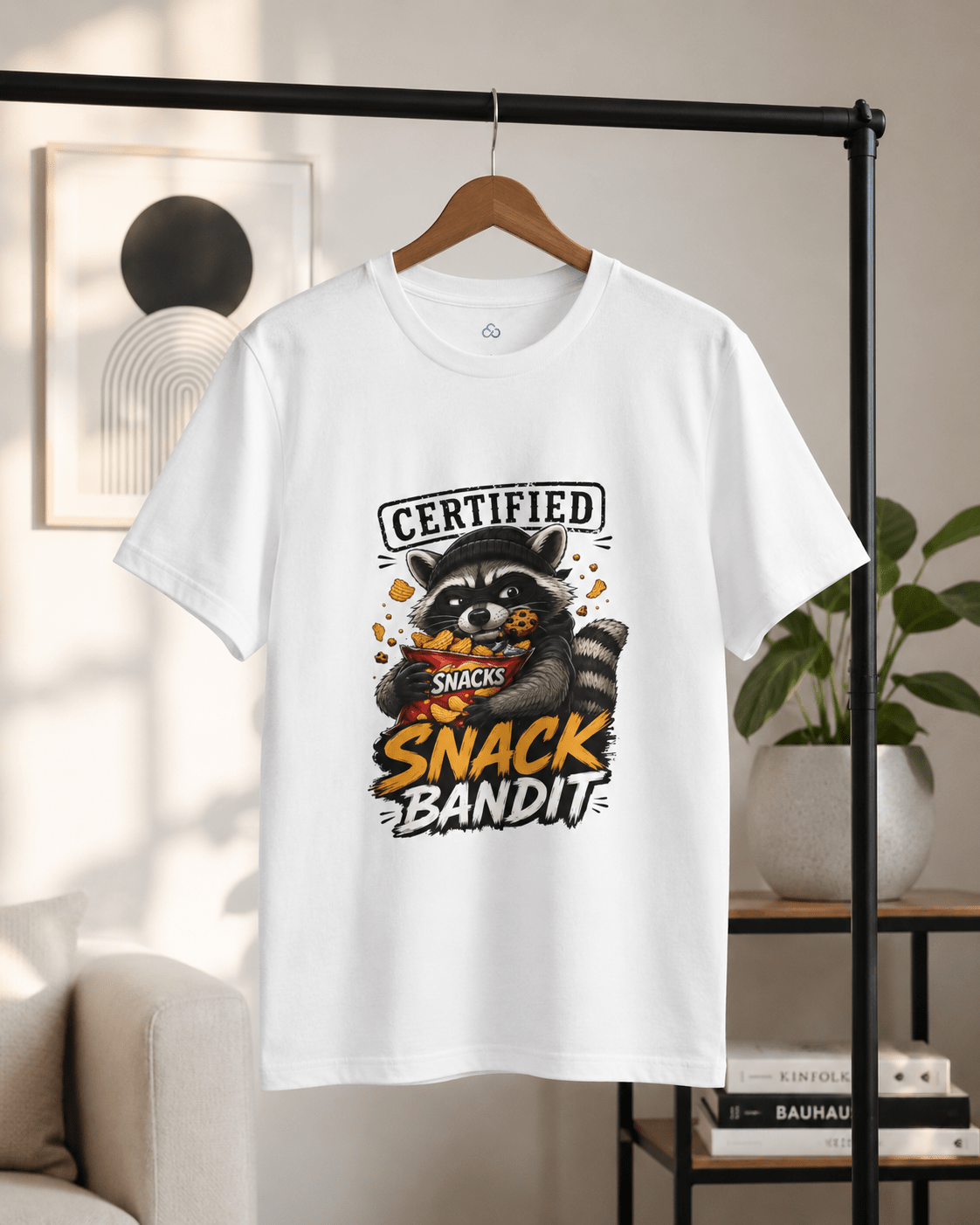 White crew-neck T-shirt hanging on a wooden hanger, raccoon 'Snack Bandit' print