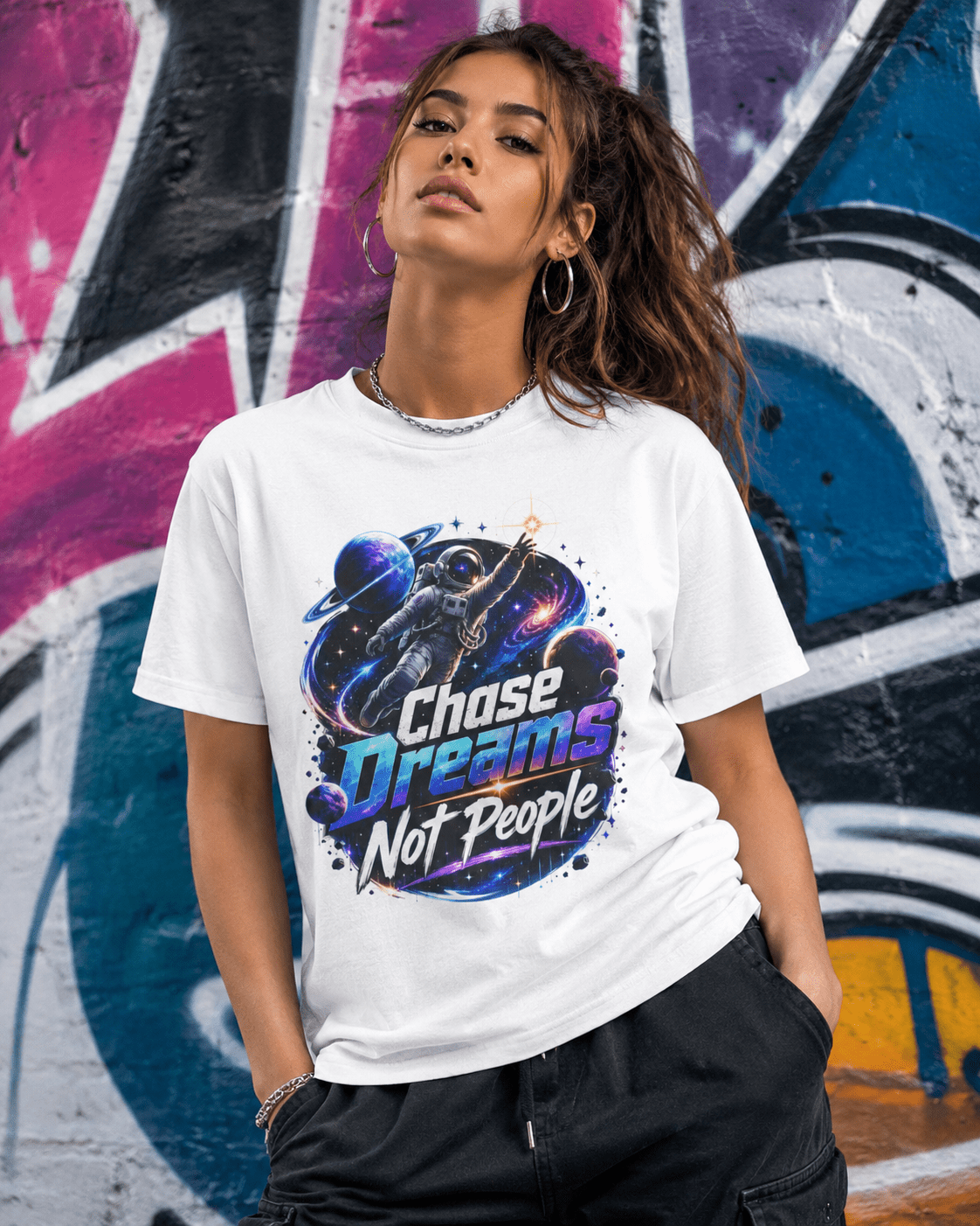 White crewneck graphic T-shirt on person, astronaut “Chase Dreams Not People” print across chest.