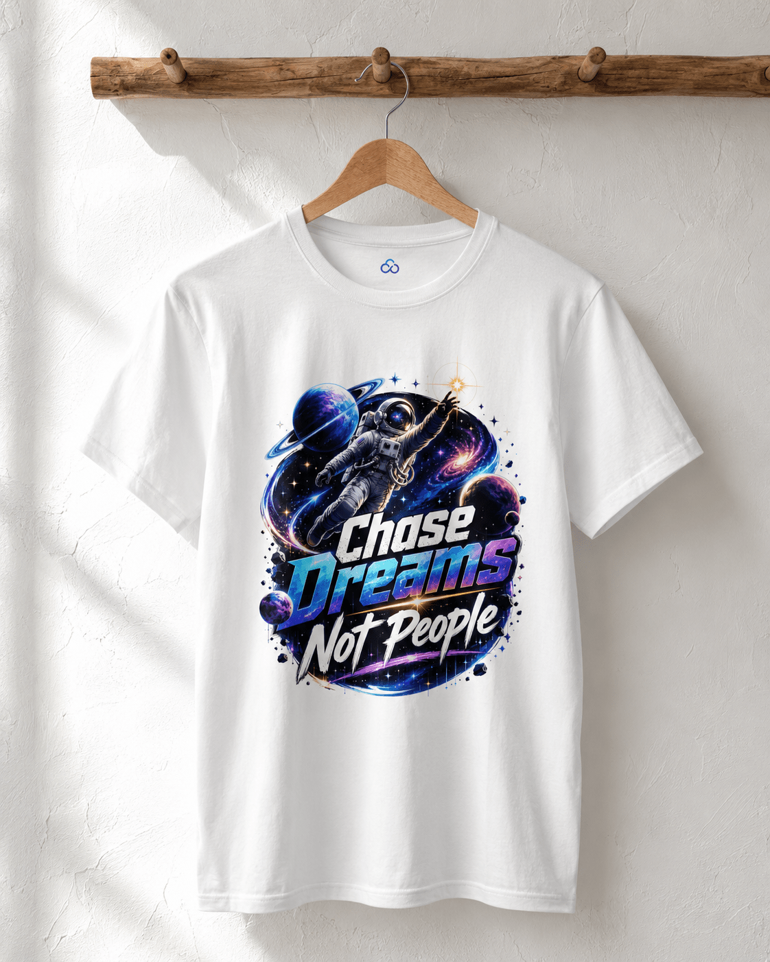 White crewneck T-shirt hanging on wooden hanger, astronaut “Chase Dreams Not People” chest graphic.