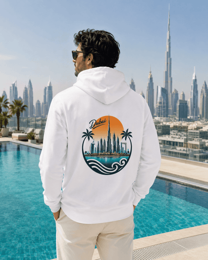 A man wearing a white hoodie with a large circular Dubai cityscape graphic on the back, standing by a swimming pool with a city skyline in the background.