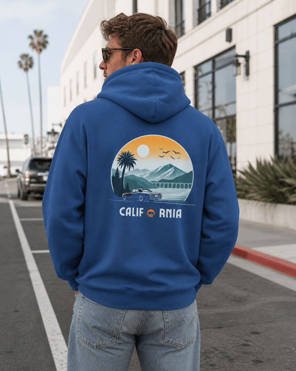Man wearing a blue hoodie with a California-themed graphic on the back, standing on a street.