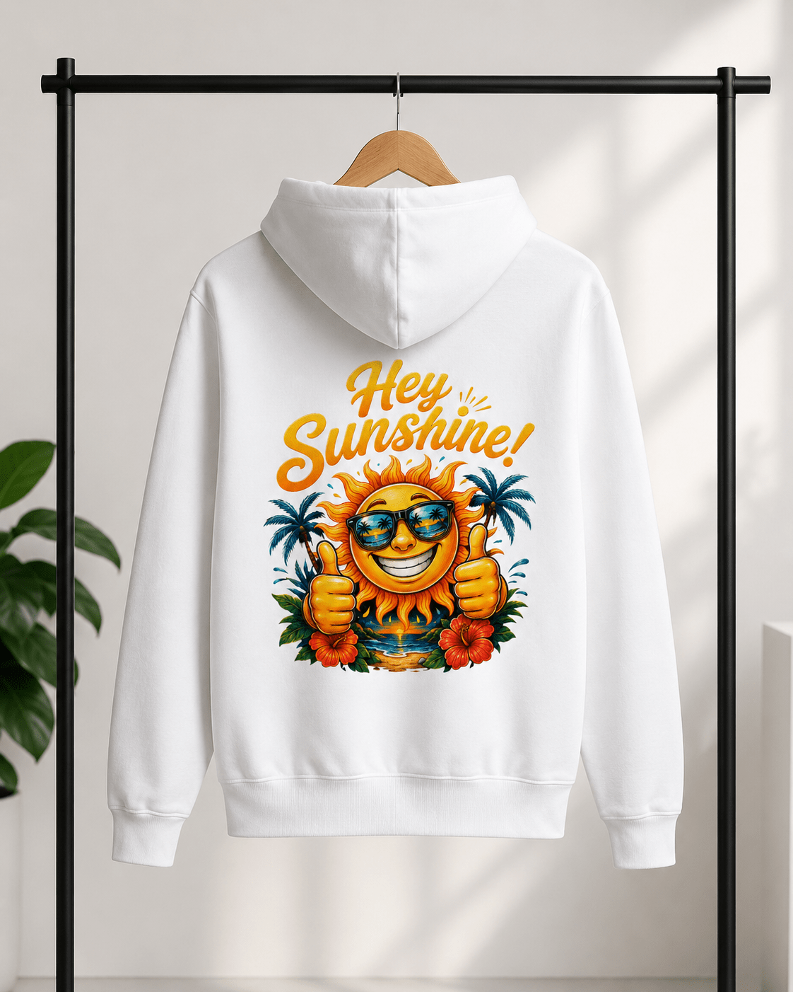 A white pullover hoodie hanging on a wooden hanger against a light wall, with a colorful graphic on the back featuring a smiling sun wearing sunglasses, palm trees, flowers, and the words 'Hey Sunshine!' in orange script.
