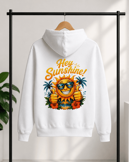 A white pullover hoodie hanging on a wooden hanger against a light wall, with a colorful graphic on the back featuring a smiling sun wearing sunglasses, palm trees, flowers, and the words 'Hey Sunshine!' in orange script.