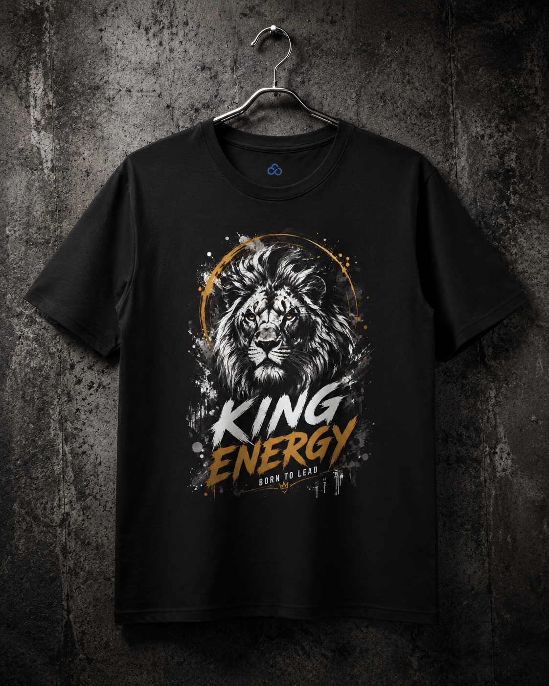 A black short-sleeve t-shirt hanging on a metal hanger against a dark textured wall. The shirt features a graphic print of a lion's face inside a gold circular frame, with the words 'KING ENERGY' in white and gold distressed lettering, and 'BORN TO LEAD' below it.