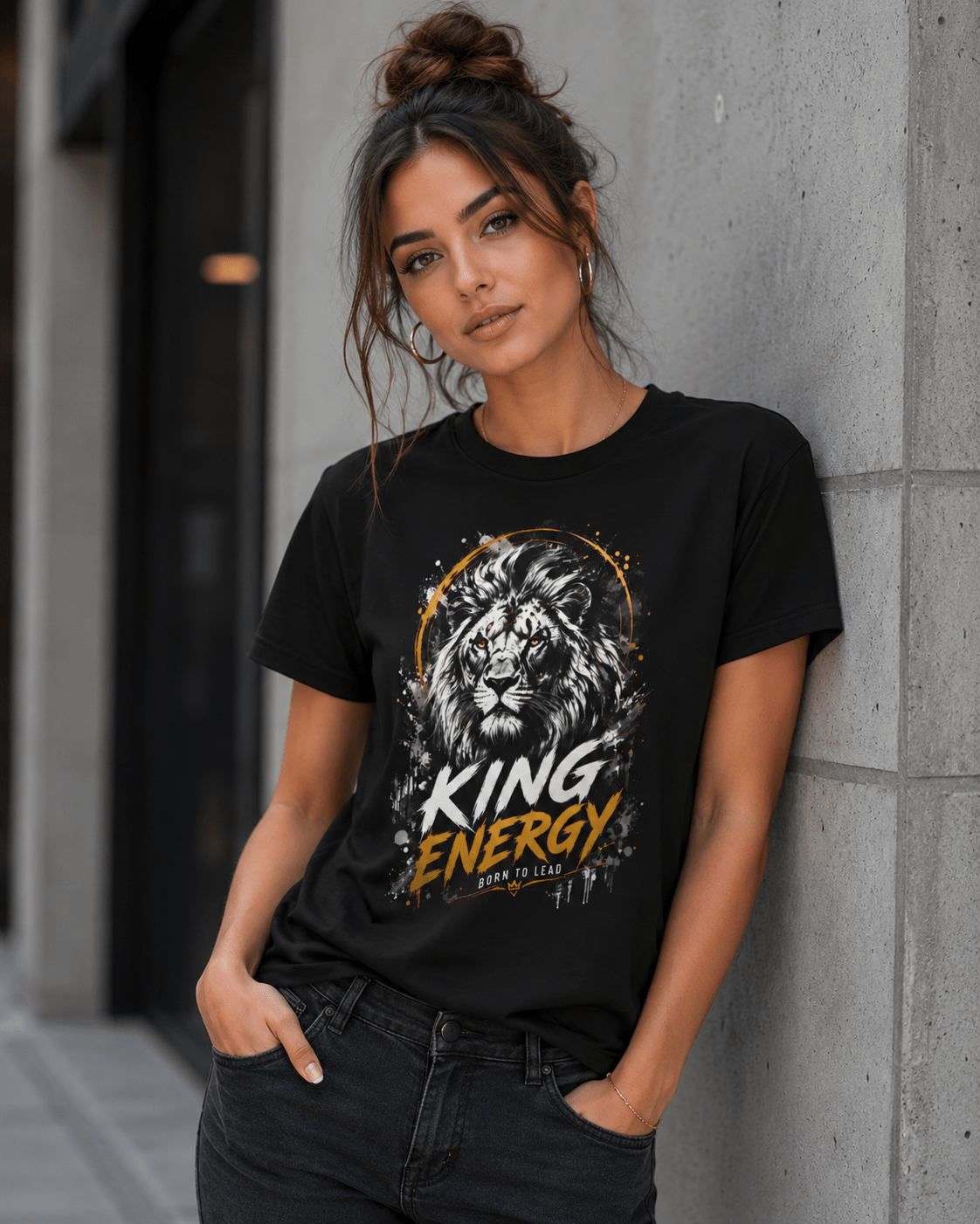 Woman wearing a black t-shirt with a lion graphic and 'KING ENERGY' text, standing against a concrete wall.