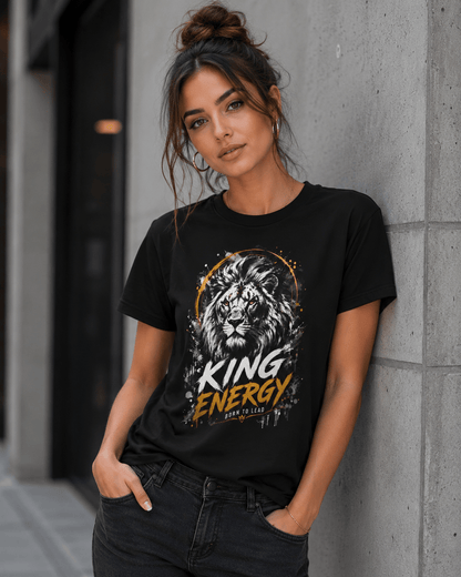 Woman wearing a black t-shirt with a lion graphic and 'KING ENERGY' text, standing against a concrete wall.