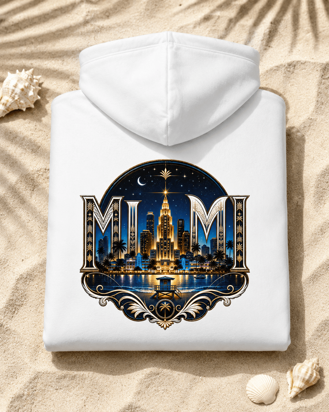 A white hooded sweatshirt laid flat on sandy ground with seashells nearby. The front has a large decorative graphic featuring the letters 'MIM' and a nighttime city skyline with a tall illuminated building, stars, moon, and water reflection.