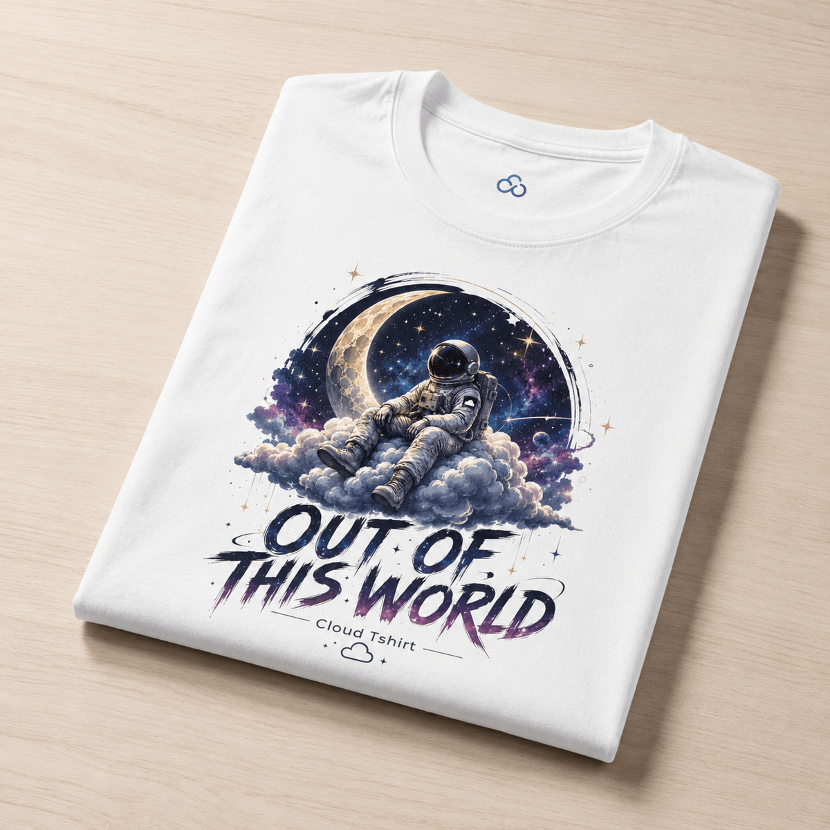 A folded white t-shirt with a colorful graphic of an astronaut floating in space above clouds and a crescent moon, with the text 'OUT OF THIS WORLD' and 'Cloud Tshirt' printed below, displayed on a light wood background.