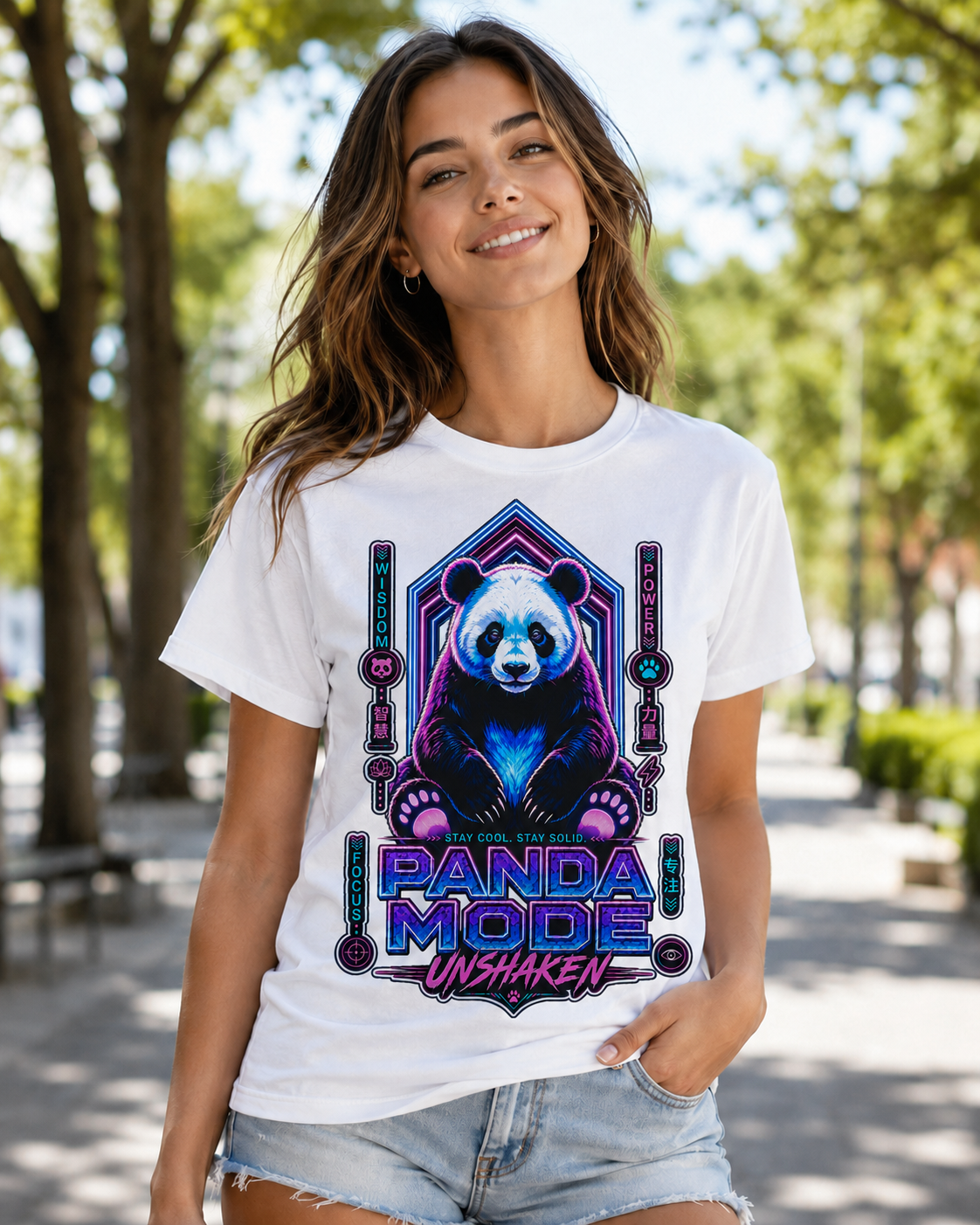 A woman wearing a white graphic t-shirt with a colorful 'Panda Mode Unshaken' design featuring a panda in neon purple and blue, set against a blurred outdoor park background.