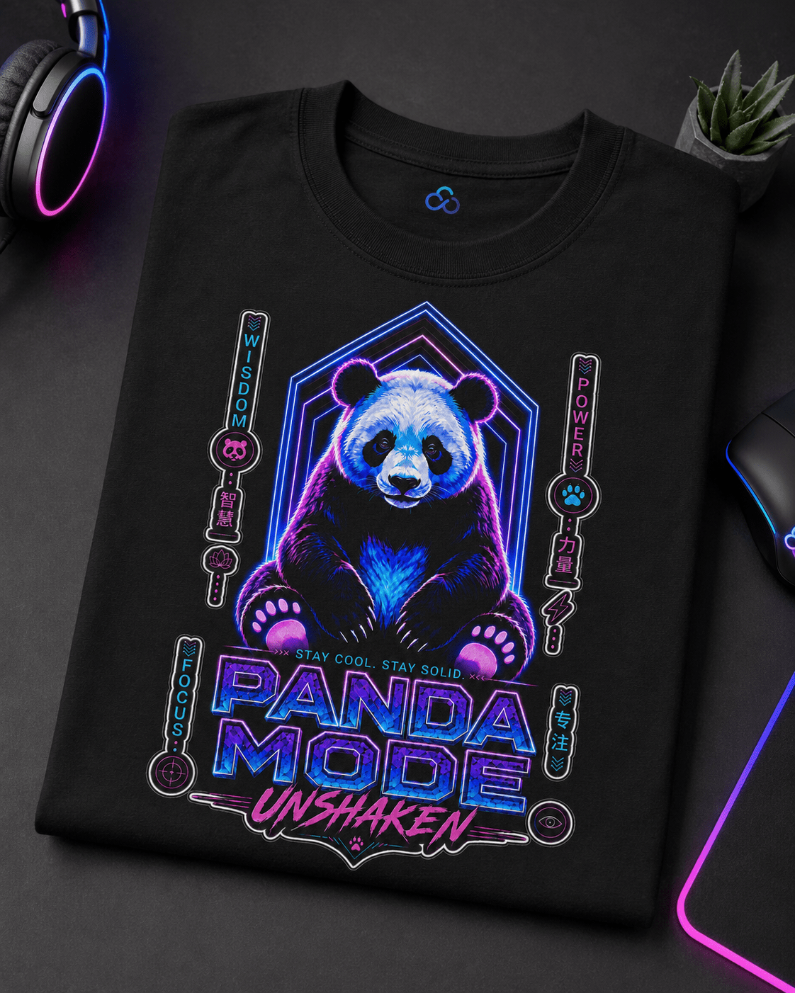 A black short-sleeve t-shirt with a colorful graphic of a panda bear and the text 'PANDA MODE UNSHAKEN' in neon blue and pink, displayed on a dark desk with gaming accessories.