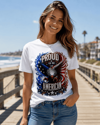 A woman wearing a white graphic t-shirt with a patriotic eagle design that reads 'PROUD TO BE AMERICAN' in red, white, and blue, standing on a wooden boardwalk by the beach.