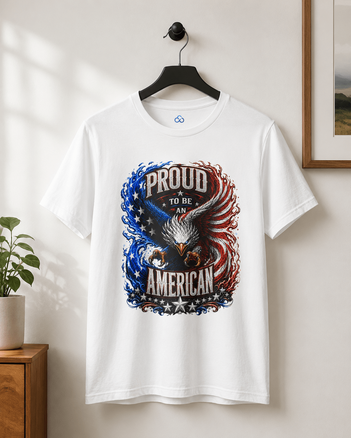 A white short-sleeve crewneck t-shirt hanging on a black hanger against a light beige wall. The shirt features a large patriotic graphic of an eagle with its wings spread, surrounded by the text 'PROUD TO BE AN AMERICAN' in distressed lettering, with blue and red flag-inspired swirls and stars.