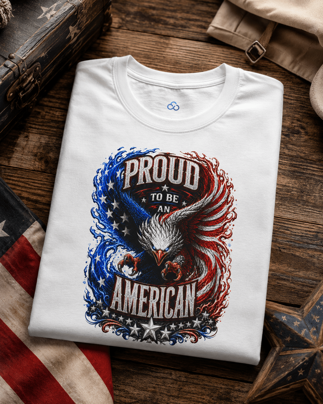 A folded white t-shirt with a patriotic graphic of an eagle and the text 'PROUD TO BE AN AMERICAN' in red, white, and blue, displayed on a rustic wooden surface with themed props.