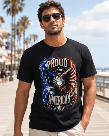 A man wearing a black graphic t-shirt with a patriotic eagle design and the text 'PROUD TO BE AN AMERICAN', standing on a sunny boardwalk with palm trees and the ocean in the background.