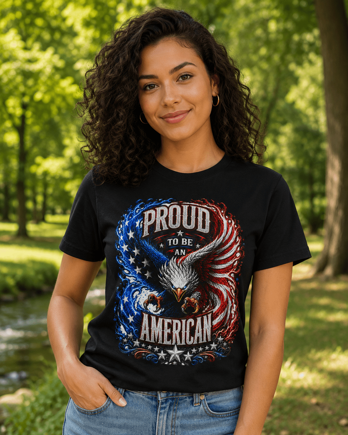 A woman wearing a black graphic t-shirt with a patriotic eagle design that reads 'PROUD TO BE AN AMERICAN' in red, white, and blue, set against a blurred green park background.