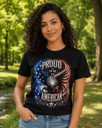 A woman wearing a black graphic t-shirt with a patriotic eagle design that reads 'PROUD TO BE AN AMERICAN' in red, white, and blue, set against a blurred green park background.