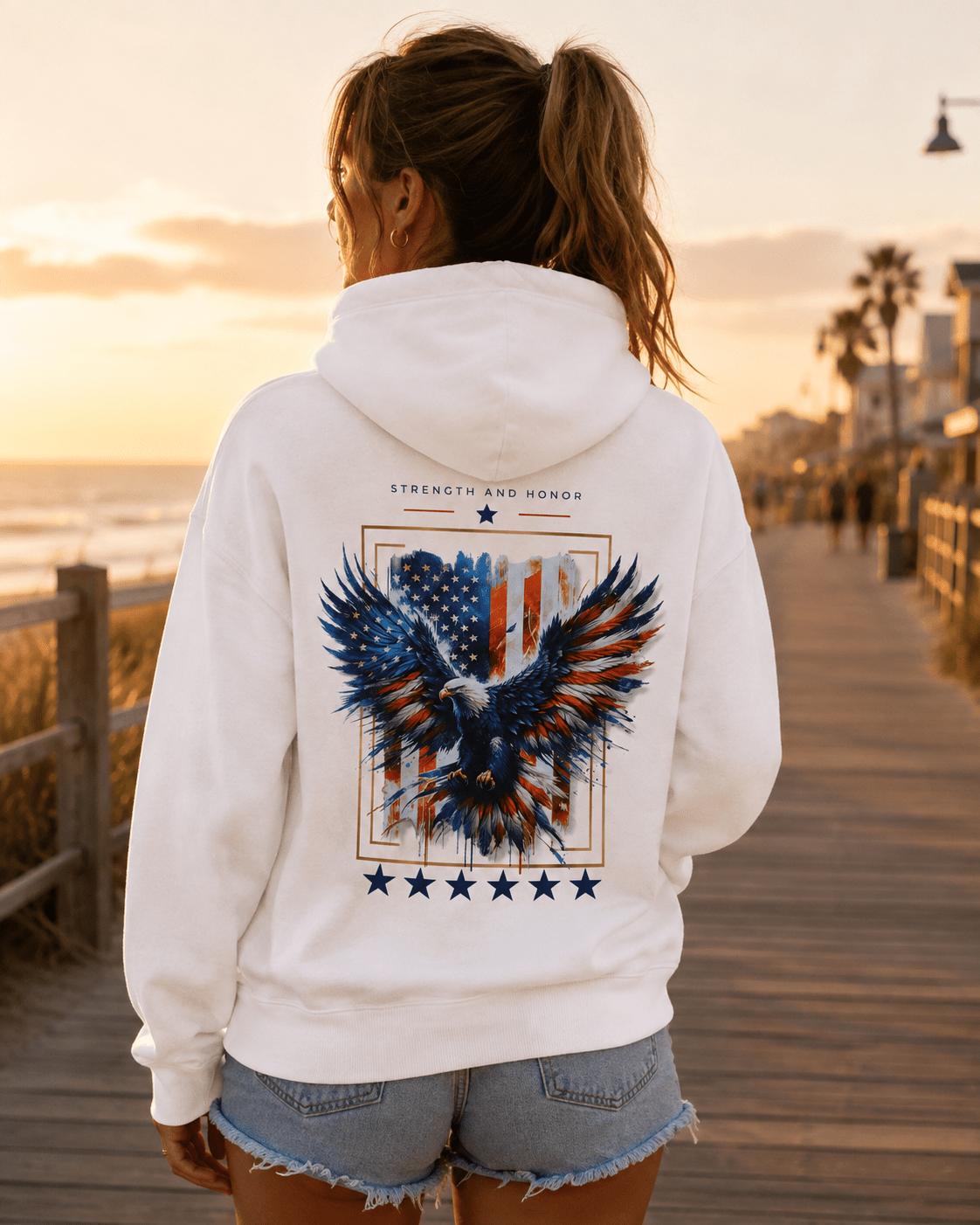 White hoodie worn outdoors, back eagle and stars graphic visible behind the hood