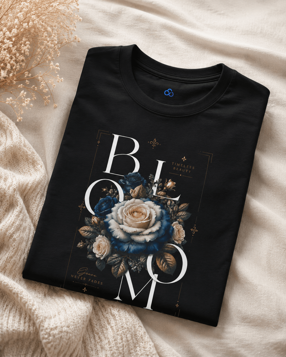Folded black t-shirt with floral design and 'BLOOM' text on a beige fabric background