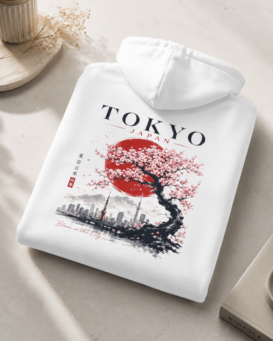 Folded white hoodie with TOKYO JAPAN cherry tree and skyline graphic on back.