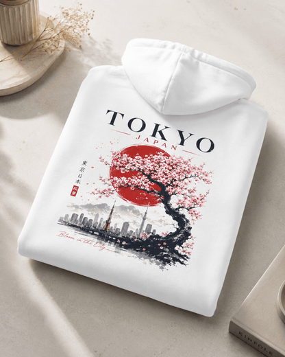 Folded white hoodie with TOKYO JAPAN cherry tree and skyline graphic on back.
