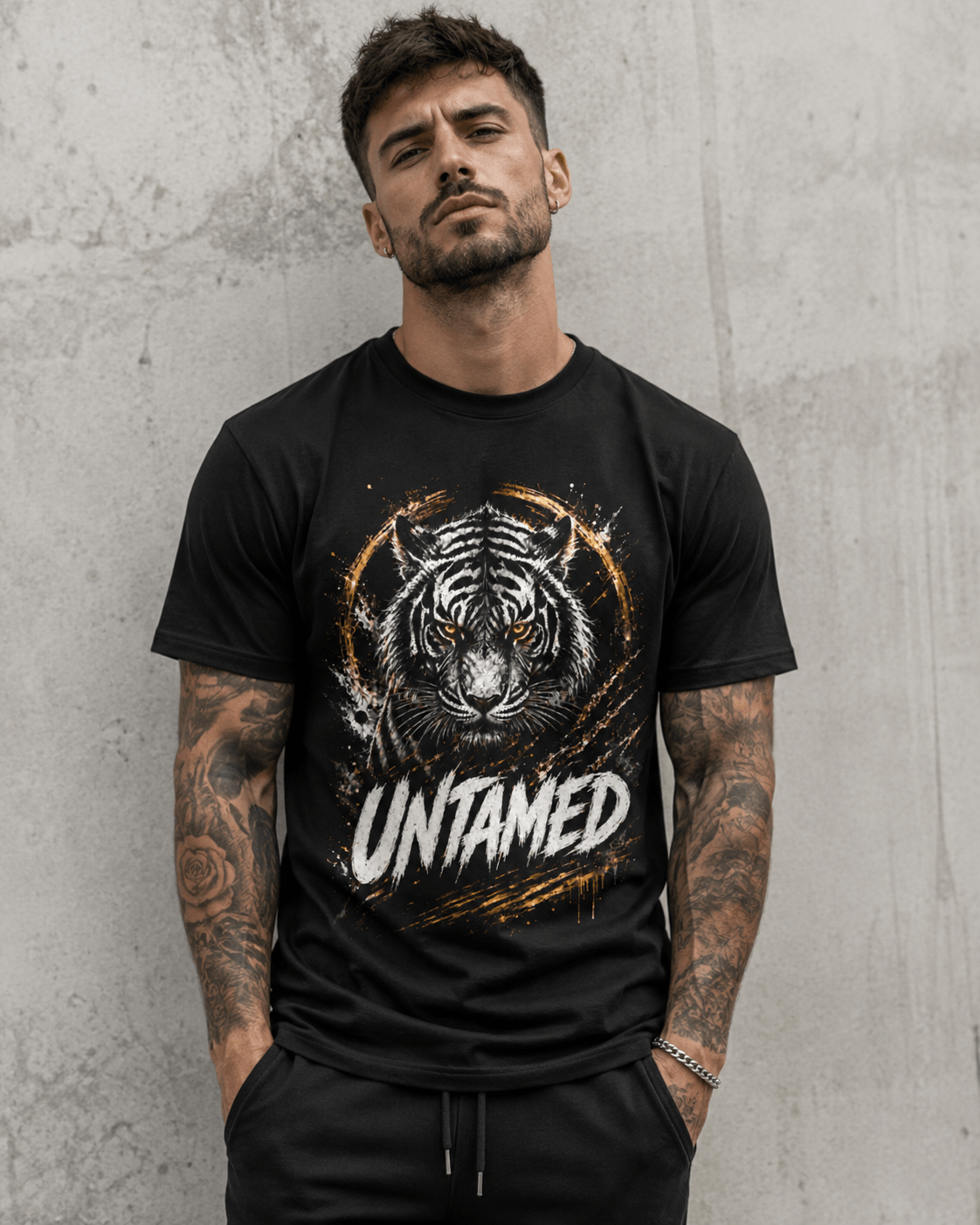 A man wearing a black short-sleeve graphic t-shirt with a tiger face print and the word 'UNTAMED' on the front, standing against a textured gray concrete wall.