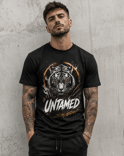 A man wearing a black short-sleeve graphic t-shirt with a tiger face print and the word 'UNTAMED' on the front, standing against a textured gray concrete wall.